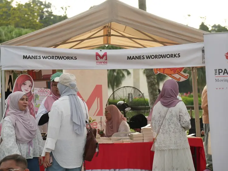 Pengunjung berbual di hadapan sebuah gerai buku berkhemah putih dengan meja penuh naskhah.