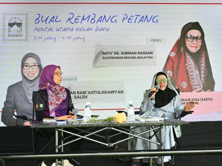 Dua orang panel duduk di meja pentas, seorang sedang bercakap ke dalam mikrofon.